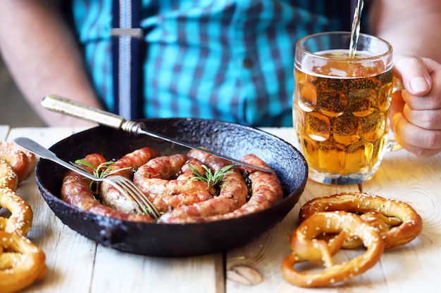 Um homem em um bar come linguiça e pretzels com cerveja.