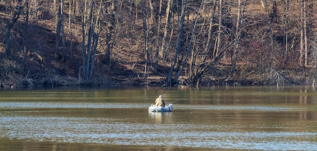Um homem em um barco está pescando em um lago em um dia claro e ensolarado
