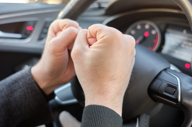 Um homem em um carro moderno. Mãos batendo no volante com raiva.