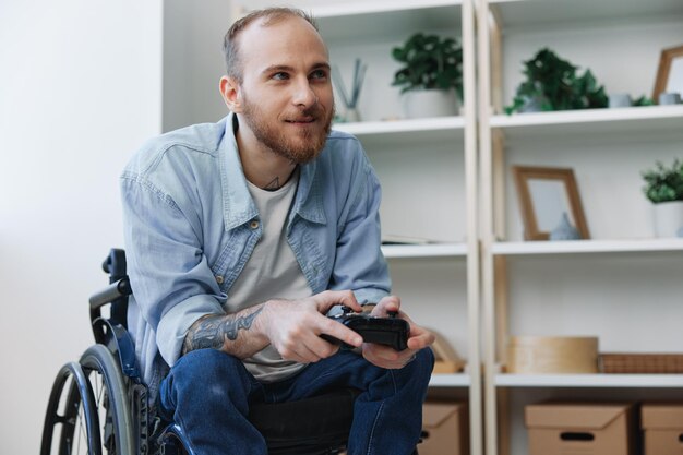 Foto um homem em um jogador de cadeira de rodas joga jogos com um joystick nas mãos em casa, descanse espaço de cópia on-line com tatuagens nos braços conceito de saúde homem com deficiência pessoa real