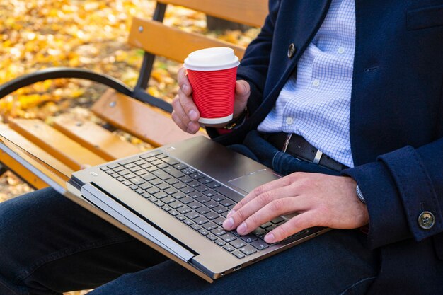 Um homem em um parque de outono em um banco com um laptop e café