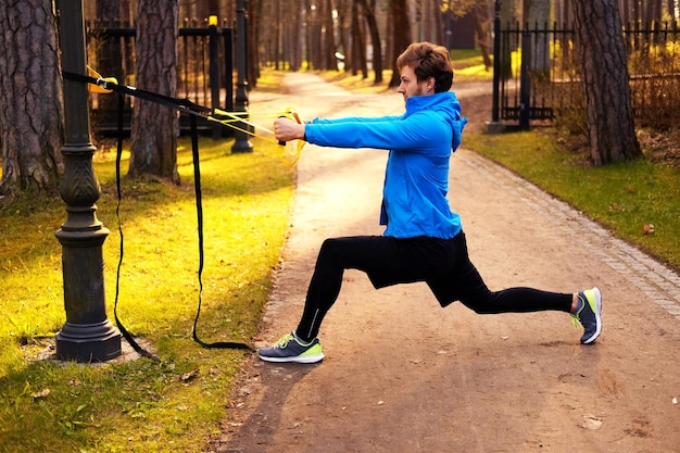 Um homem em um parque melhorando a flexibilidade das pernas com tiras de fitness trx.