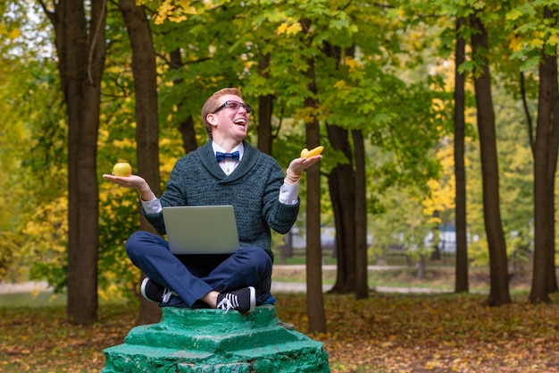 Um homem em um pedestal que finge ser uma estátua na pose de um filósofo antes de escolher uma maçã ou uma banana no parque outono