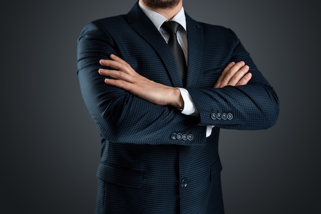 Um homem em um terno de negócio está com os braços cruzados sobre um fundo cinza.