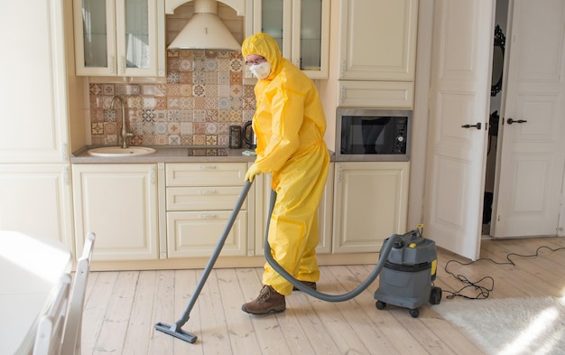 Um homem em um traje de proteção limpa a sala com um aspirador de pó