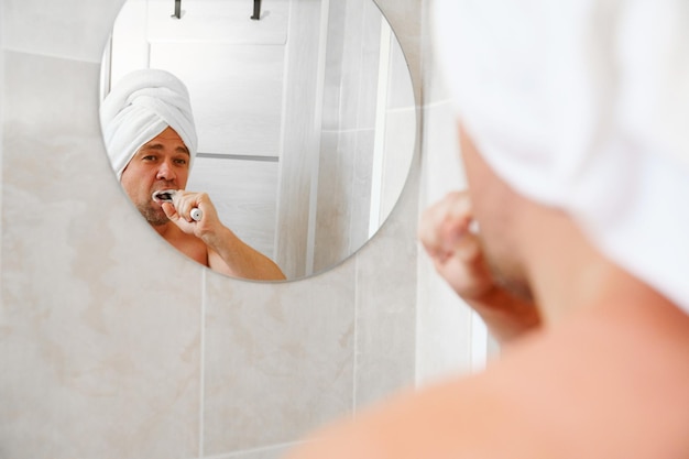 Um homem em um turbante feito de uma toalha na cabeça escova os dentes depois de um banho matinal