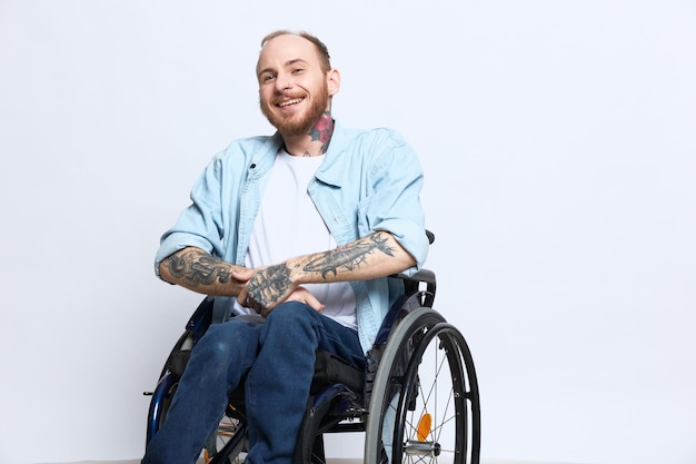 Foto um homem em uma cadeira de rodas e apontando o dedo para o espaço da cópia com tatuagens nas mãos senta-se em um estúdio cinza conceito de saúde uma pessoa com deficiência uma pessoa real