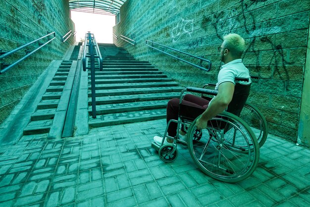 Foto um homem em uma cadeira de rodas está sentado no fundo da escada. os dias cinzentos dos deficientes, problemas de movimento, doenças.