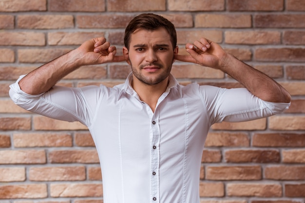 Um homem em uma camisa branca perto de uma parede de tijolos.