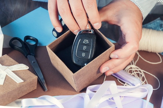 Um homem em uma camisa leve está preparando uma caixa de presente para o feriado. tonificação o carro como presente. chaves do carro na caixa de presente.