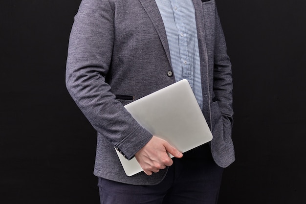 Um homem em uma jaqueta segurando um laptop em um espaço preto.