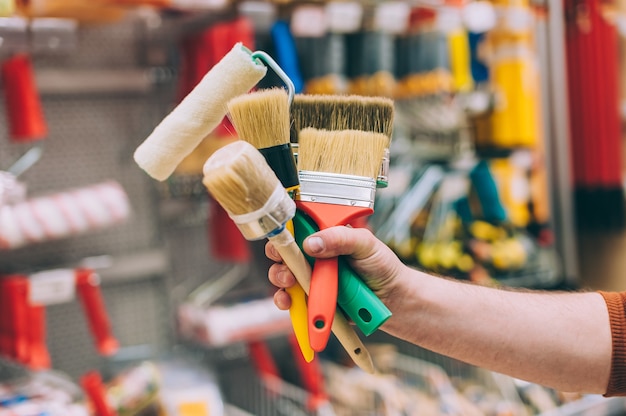 Foto um homem em uma loja de ferragens segura um conjunto de pincéis e rolos para pintura e decoração.