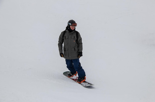 Um homem em uma prancha de snowboard desce a encosta da montanha