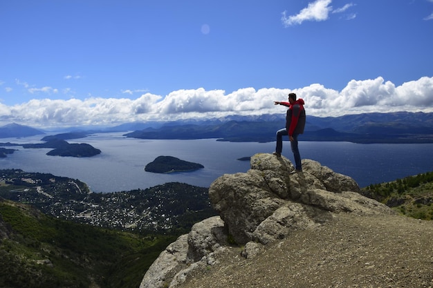 Um homem em uma rocha observa a paisagem na vista de San Carlos de Bariloche do lago e da cidade de Bariloche