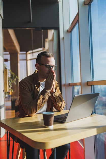 Um homem equilibrado de óculos e roupas casuais trabalha em um laptop em um espaço de trabalho aconchegante Um freelancer de sucesso trabalha remotamente
