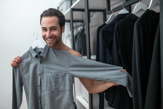 Um homem escolhendo roupas e segurando uma camisa cinza nas mãos