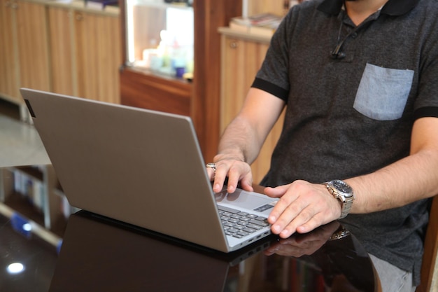 Um homem está digitando em um laptop com capa cinza.