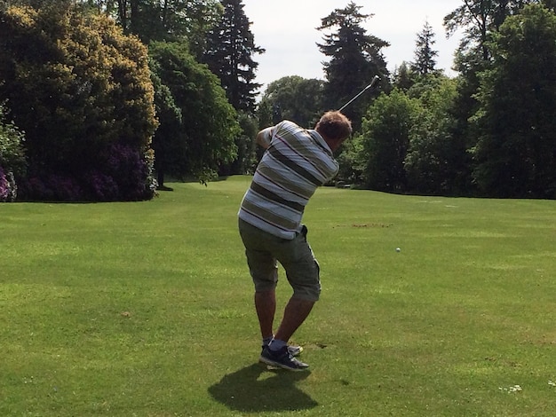 Um homem está jogando golfe em um belo campo de golfe verde ensolarado Acerta a bola de golfe à distância