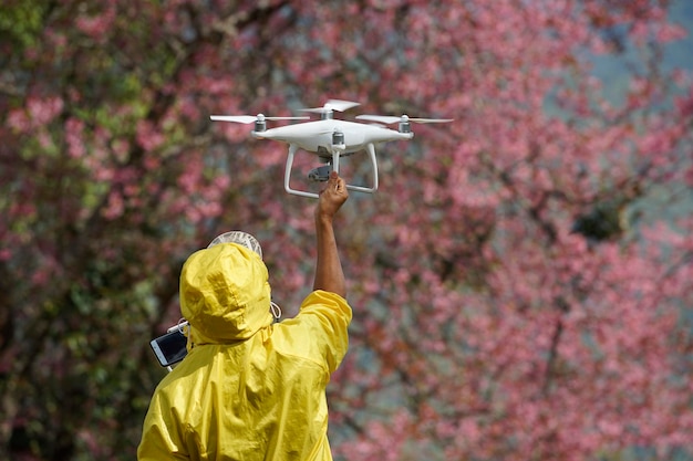 Um homem está lançando um drone com flor rosa borrada no fundo