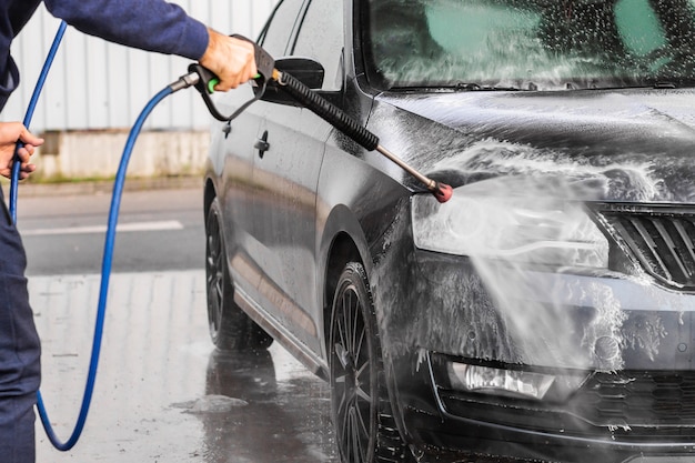 Um homem está lavando um carro na lavagem de carros self-service. Máquina de lavar a alta pressão do veículo pulveriza espuma