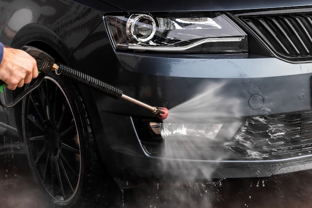 Um homem está lavando um carro na lavagem de carros self-service. Máquina de lavar veículos de alta pressão limpa com água. Equipamento de lavagem de carro, Mlada Boleslav,