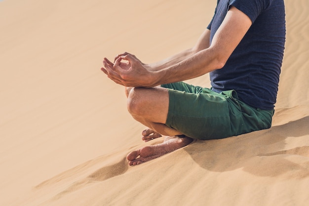 Um homem está meditando na areia do deserto