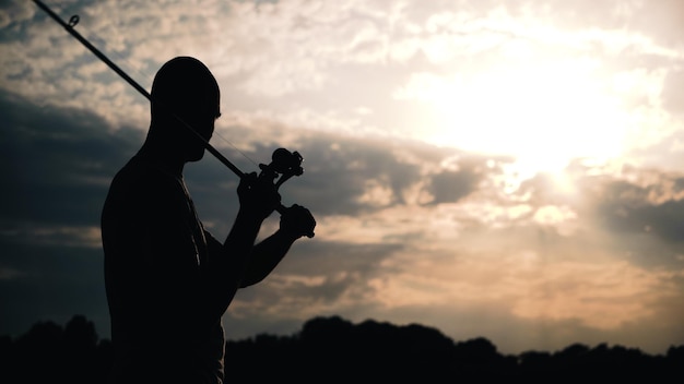 Um homem está pescando no pôr do sol do lago descansando na natureza