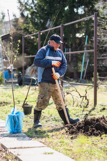 Um homem está plantando uma árvore jovem o agricultor está cavando o chão com uma pá para uma pequena muda o conceito de proteção do meio ambiente e ecologia