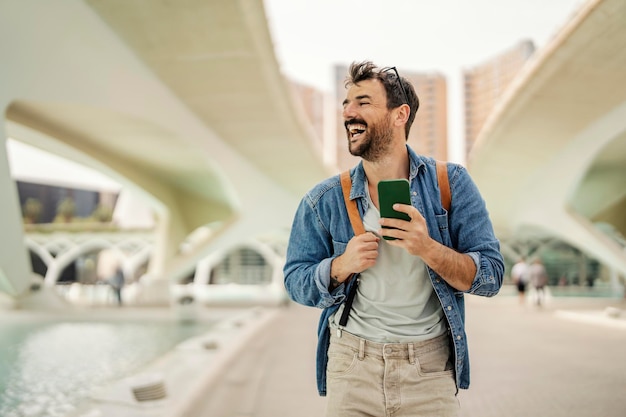 Um homem está rindo na rua da cidade enquanto caminha e usa o telefone