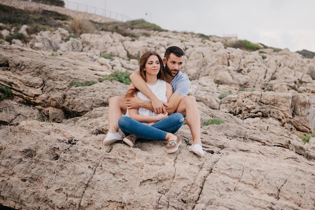 Um homem está segurando sua namorada enquanto ambos estão sentados nas rochas na Espanha