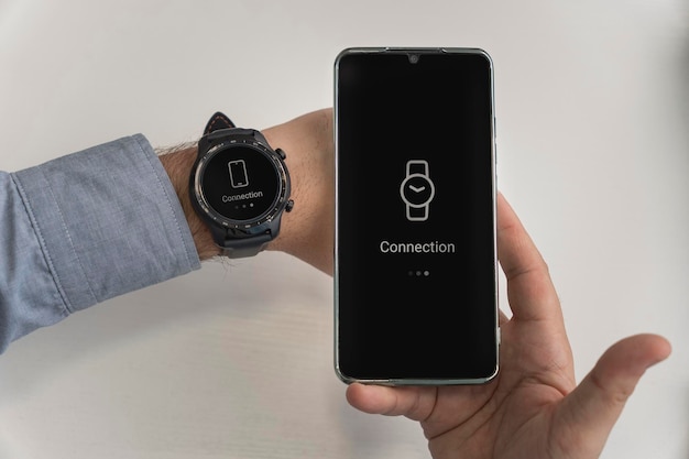 Um homem está segurando um smartphone e um smartwatch na mão conexão sem fio do relógio e telefone celular smart watch wi-fi conectar