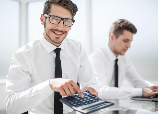 Um homem está sentado à mesa do escritório segurando uma calculadora