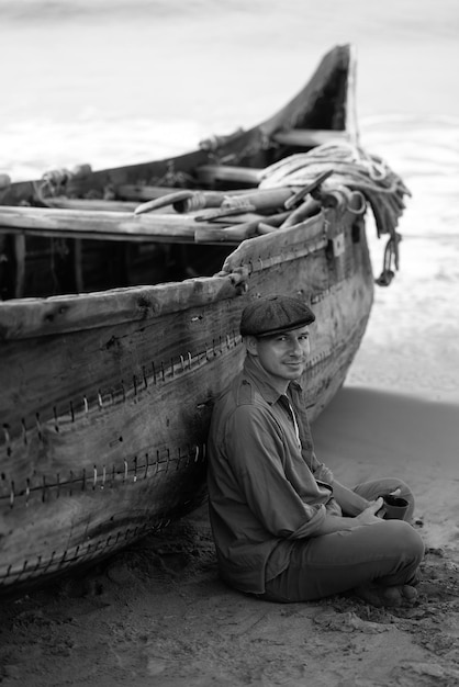 Um homem está sentado ao lado de um barco que tem a palavra mar.