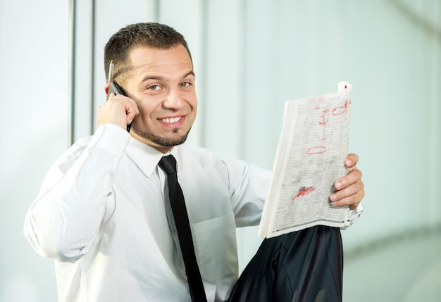 Um homem está sentado com um jornal e falando por telefone.