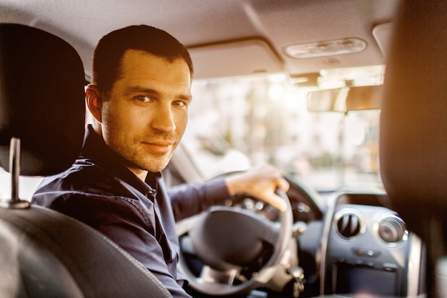 Um homem está sentado no interior de um carro e olhando para a câmera e sorrindo. Conceito de transporte.