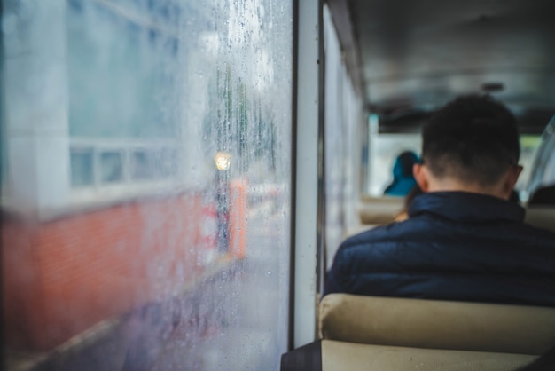 Um homem está sentado no ônibus perto de uma janela de vidro