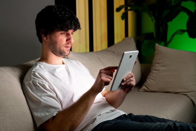 Um homem está sentado no sofá e usando um tablet de computador para navegar na internet ou fazer compras online v