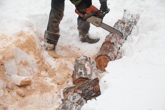 Um homem está serrando um tronco com uma serra elétrica na neve no inverno