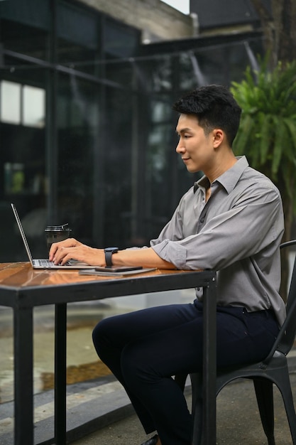 Um homem está usando seu laptop e sentado em uma cafeteria em um espaço ao ar livre