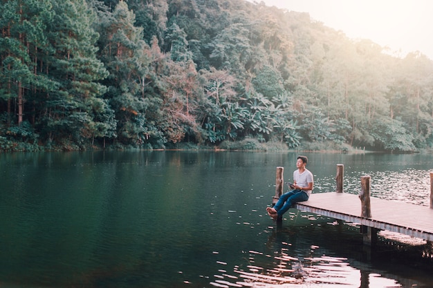 Um homem estava relaxando na ponte de madeira na beira do lago na parte da tarde.