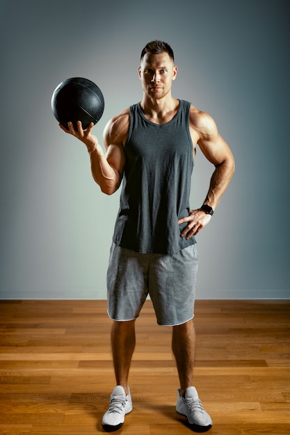 Foto um homem faz exercícios com uma fitball em um fundo cinza.