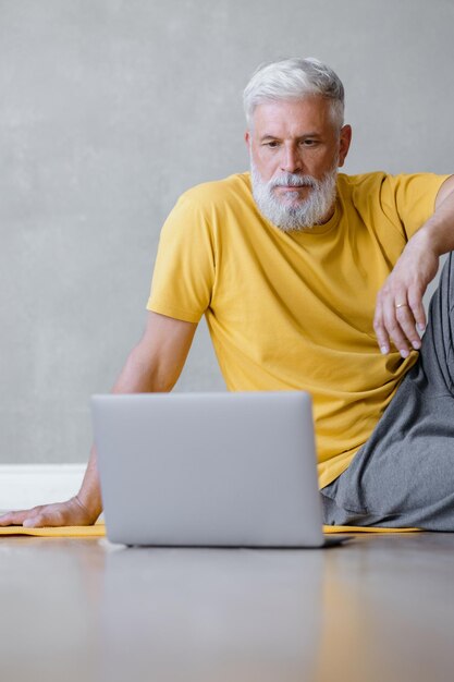 Um homem faz ioga e fitness no ginásio com um treinador on-line de um treinador de esportes masculino sênior de laptop