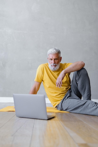 Um homem faz ioga e fitness no ginásio com um treinador on-line de um treinador de esportes masculino sênior de laptop