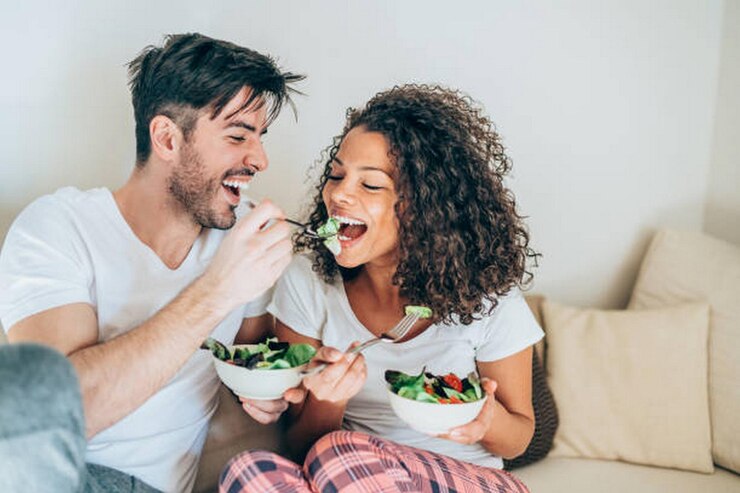 Foto um homem feliz a alimentar a namorada com salada.