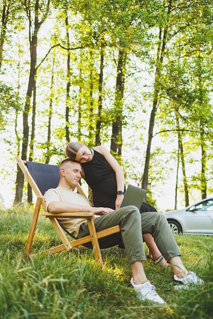 Um homem feliz e sua esposa grávida estão trabalhando em um laptop enquanto estão sentados na natureza Um jovem casal está relaxando na natureza e assistindo a um filme em um laptop