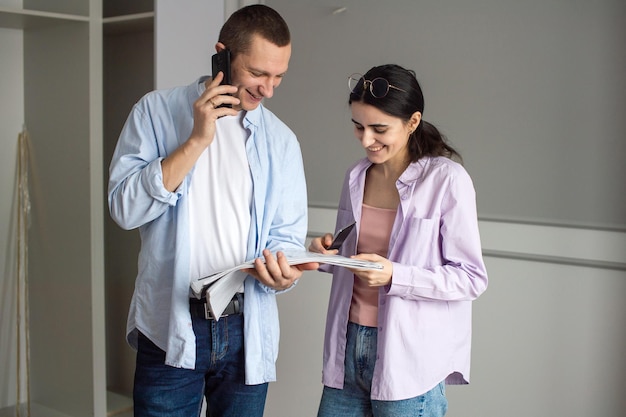 Um homem feliz está falando ao telefone, uma mulher está olhando os desenhos de um novo apartamento