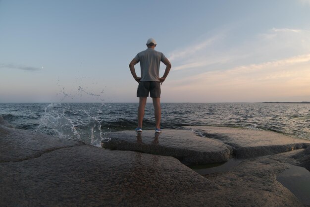 Um homem fica em uma praia rochosa e olha para o horizonte Vista de trás