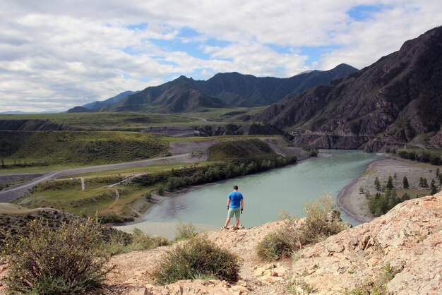 Um homem fica na beira de uma montanha e olha para uma bela paisagem montanhosa de uma altura