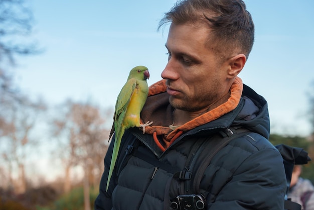 Um homem forma uma ligação com um papagaio verde durante o inverno em um parque de Londres