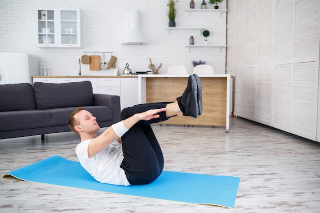 Um homem forte e atlético em uma camiseta e fazendo exercícios de imprensa em casa em seu apartamento espaçoso e bem iluminado com um interior minimalista. Praticar esportes em casa.